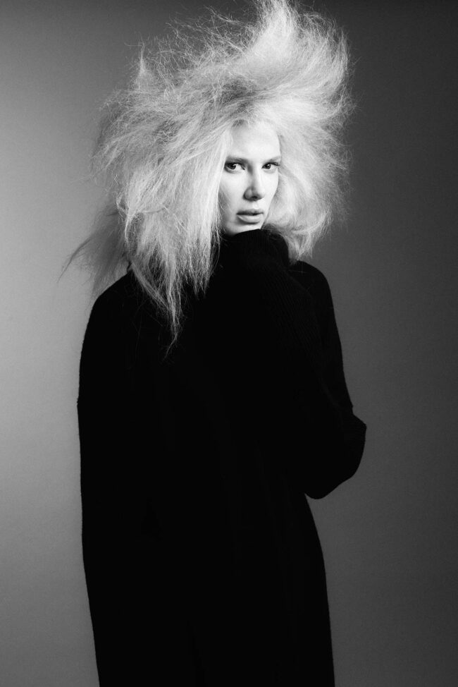Los Angeles fashion photographer, black and white beauty fashion image of a model with voluminous platinum hair wearing a black turtleneck against a gray studio backdrop, editorial photo for fashion brands, beauty campaigns, lookbooks, and digital marketing.