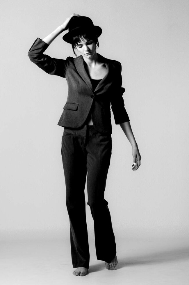 Los Angeles fashion photographer, black and white studio fashion image of a model in a tailored suit and hat with minimal posing and clean negative space, editorial photo for fashion brands, lookbooks, and digital marketing.