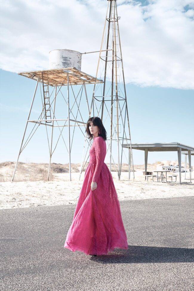 Los Angeles fashion photographer, location-based editorial fashion image of a model in a bright pink lace dress standing near a water tower and open landscape, campaign photo for fashion brands, lookbooks, and digital marketing.