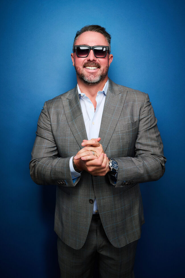 Social media photographer in Los Angeles, confident personal brand portrait of a man in a gray suit and sunglasses against a blue studio backdrop, content photo for Instagram, websites, and digital marketing.