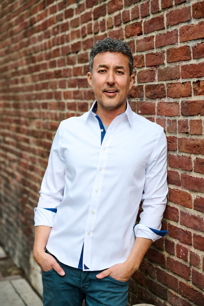 Social media photographer in Los Angeles, urban personal brand portrait of a man in a white button-up shirt leaning against a brick wall, lifestyle content photo for Instagram, websites, and digital marketing.